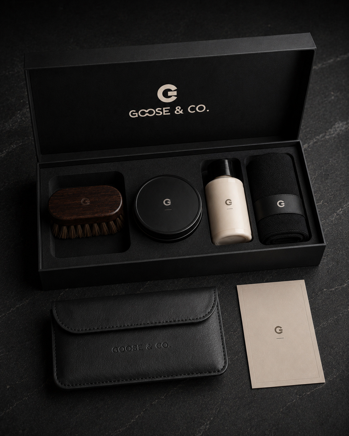 The Ownership Ritual presentation box, opened to reveal leather care implements, beside a leather pouch and printed card on a dark stone surface.